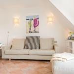 Living room with sofa, wall art, and terracotta floor under sloped ceiling.