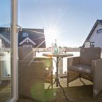 Terrace with two chairs and table. Sun shining. Background: houses.