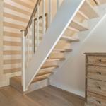 Staircase with wooden steps, white balustrade, and striped wall
