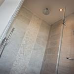 Shower area with glass wall, stone tiles, and shower head on the ceiling.