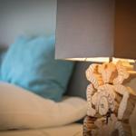 Nightstand lamp with wooden figure beside bed with pillows.
