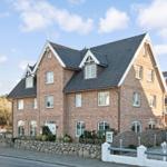Brick house with dark roof and white window frames. Forecourt with stone wall and paved area.