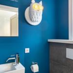 Badezimmer mit blauen Wänden, Spiegel, Waschbecken und Eule-Lampe.