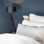 Bettkopfteil mit Kissen und Nachttischlampe vor blauer Wand