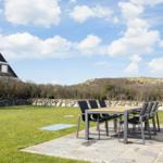 Hinterhof mit Tisch und Stühlen, Grasfläche und Steinmauer. Blick auf Dünen im Hintergrund.