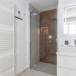 Dusche mit Glaswand, Waschbecken und Heizung.