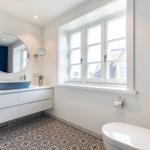 Badezimmer mit blauem Waschbecken, runden Spiegel und Fenster