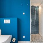 Badezimmer mit blauer Wand, Toilette und Dusche mit Glaswand.