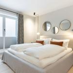 Schlafzimmer mit Doppelbett, runden Spiegeln und Fenster mit Vorhängen.