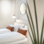 Schlafzimmer mit Bett, Kissen, Spiegel und Lampe.