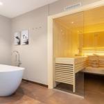 Bad mit freistehender Badewanne und Sauna im Hintergrund.