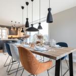 Essbereich mit Holztisch und Stühlen, Küchenbereich im Hintergrund, moderne Pendelleuchten.