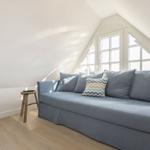 A room with a gray sofa, a wooden stool, and a TV under a skylight window.