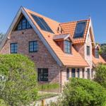 Two-story brick house with red tiled roof and solar panels.