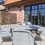 Terrace with round table and four chairs in front of brick house with windows.