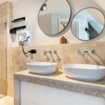 Bathroom with shower, two sinks, and round mirrors on the wall.