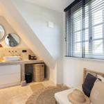 Double sink with mirrors, window with blinds, and seating with cushions.