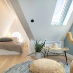 Bedroom with sloped ceiling, bed, plant, and seating under skylight.