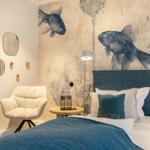Bedroom with fish-themed wall, blue bed, and white chairs.