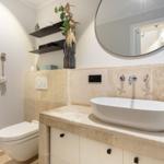 Bathroom with sink, mirror, and toilet. Stone wall and modern faucets.