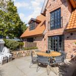 Terrace with garden lounger, table and chairs in front of brick house with dormers.