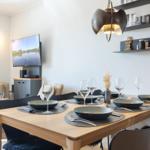 Dining table with six chairs and cutlery. Wall shelves and TV in the background.