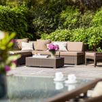 Terrace with seating, flowers, and glass table. Background: green hedge and brick wall.