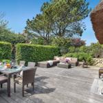 Terrace with seating area, dining table, and garden. Wooden deck, hedge, and tree visible.