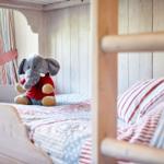 A crib bed with pillows and a stuffed toy. In the background, a window with curtains.