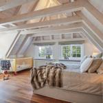 Bedroom with wooden beam ceiling, bed, crib, and windows.