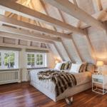 Bedroom with hardwood floor, sloped ceiling, and two windows.