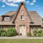 House with thatched roof, brick facade, and paved driveway with flower beds.