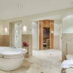 Bath with whirlpool, shower, and sauna. White bathtub, wooden sauna, and mosaic tiles.