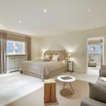 Bedroom with bed, sofa, and TV. Corridor leads to another room with window.