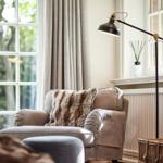 An armchair with a fur cushion is positioned in front of a window with curtains.