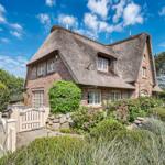 House with thatched roof, stone wall, and garden with flowers.