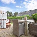 Terrasse mit Esstisch, Stühlen und Strandkorb. Hintergrund: Haus mit Strohdach.