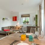Essbereich mit Tisch, Gläsern und Stühlen. Wohnbereich mit Sofa und Wandbildern.