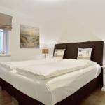 Schlafzimmer mit Bett, Nachttisch und Fenster. Wandbild zeigt Strand.