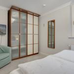 Bedroom with bed, wardrobe, armchair, and TV mounted on the wall.