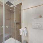 Shower with glass enclosure and shower head, white tiles and towels
