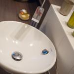 Sink with modern faucet and green bottles on countertop.