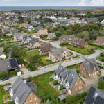 Aerial view of a coastal village with houses, gardens, and the sea in the background.