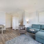 Living and dining area with blue sofa, wooden floor, and white furniture.