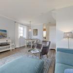 Living and dining area with sofa, armchair, and TV. Wooden floor and light walls.