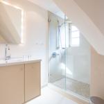 Bathroom with shower, sink, and mirror under sloped ceilings.