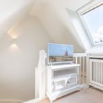 Attic room with TV and skylight. White furniture and wooden floor.