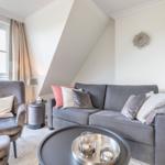 Living room with sofa, armchair, and round table under sloped ceiling.