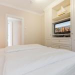Schlafzimmer mit weißem Bett und integriertem TV-Schrank