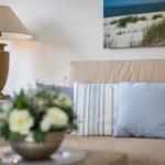 Sofa mit Kissen, Lampe und Strandbild an der Wand.